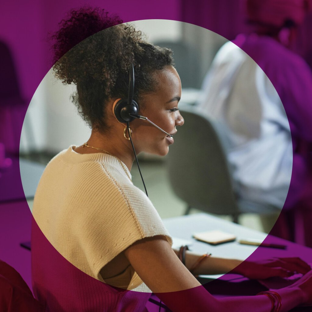 Woman providing support on the phone, she is wearing a headset and typing on a computer keyboard.